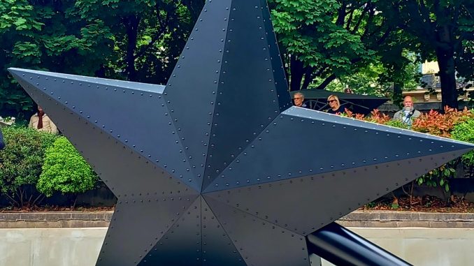 Face sombre du monument. Grande étoile (5m) noire à 5 branche. Le manche envoncé dans le sol.